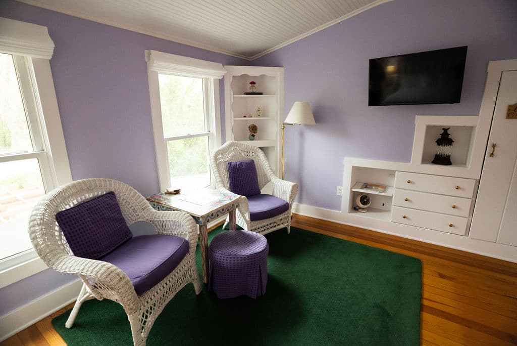 Sitting area which includes two white wicker chairs with purple cushions and flatscreen TV