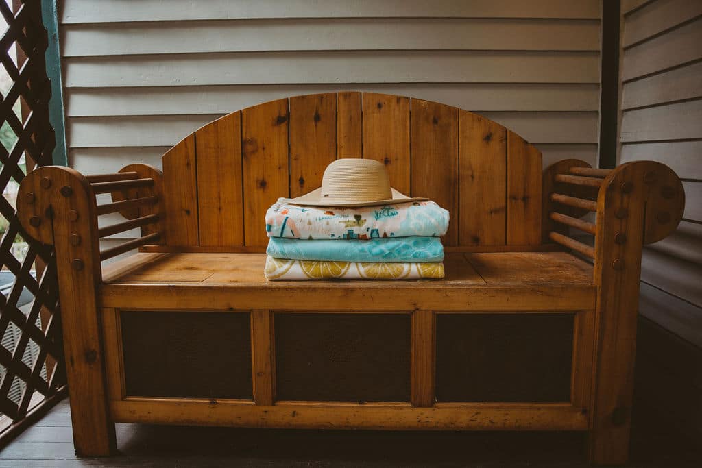 A wooden bench with neatly stacked towels and a wide-brimmed hat on top.