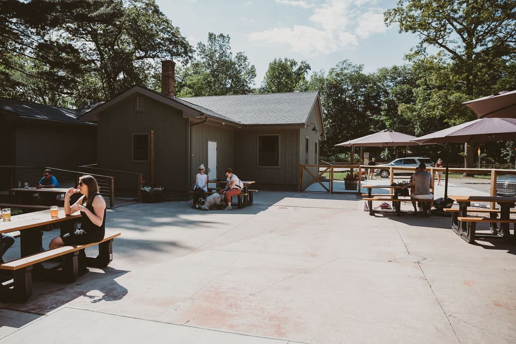 Outdoor seating area with people enjoying drinks and relaxing near a building surrounded by trees.