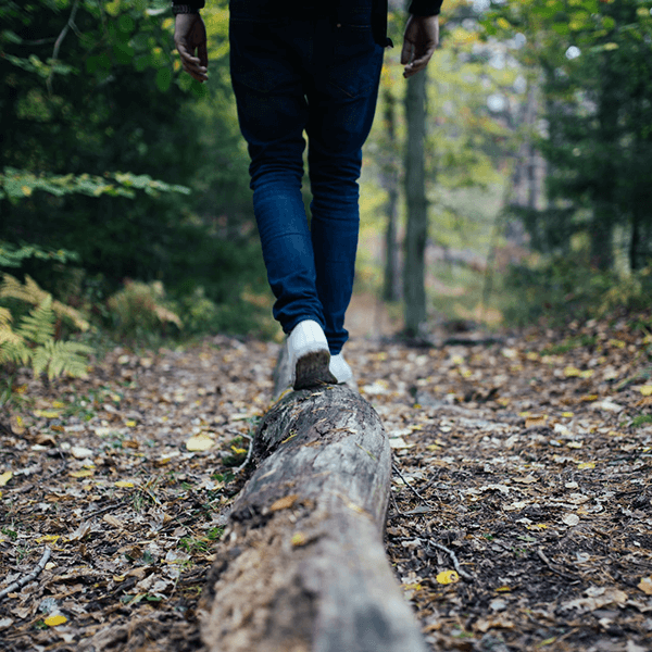 A person walks along a fallen log in a forest path.