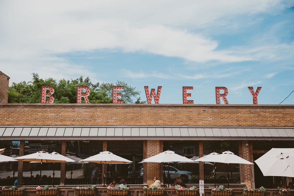 A brick building with "BREWERY" in red letters and outdoor seating under umbrellas.