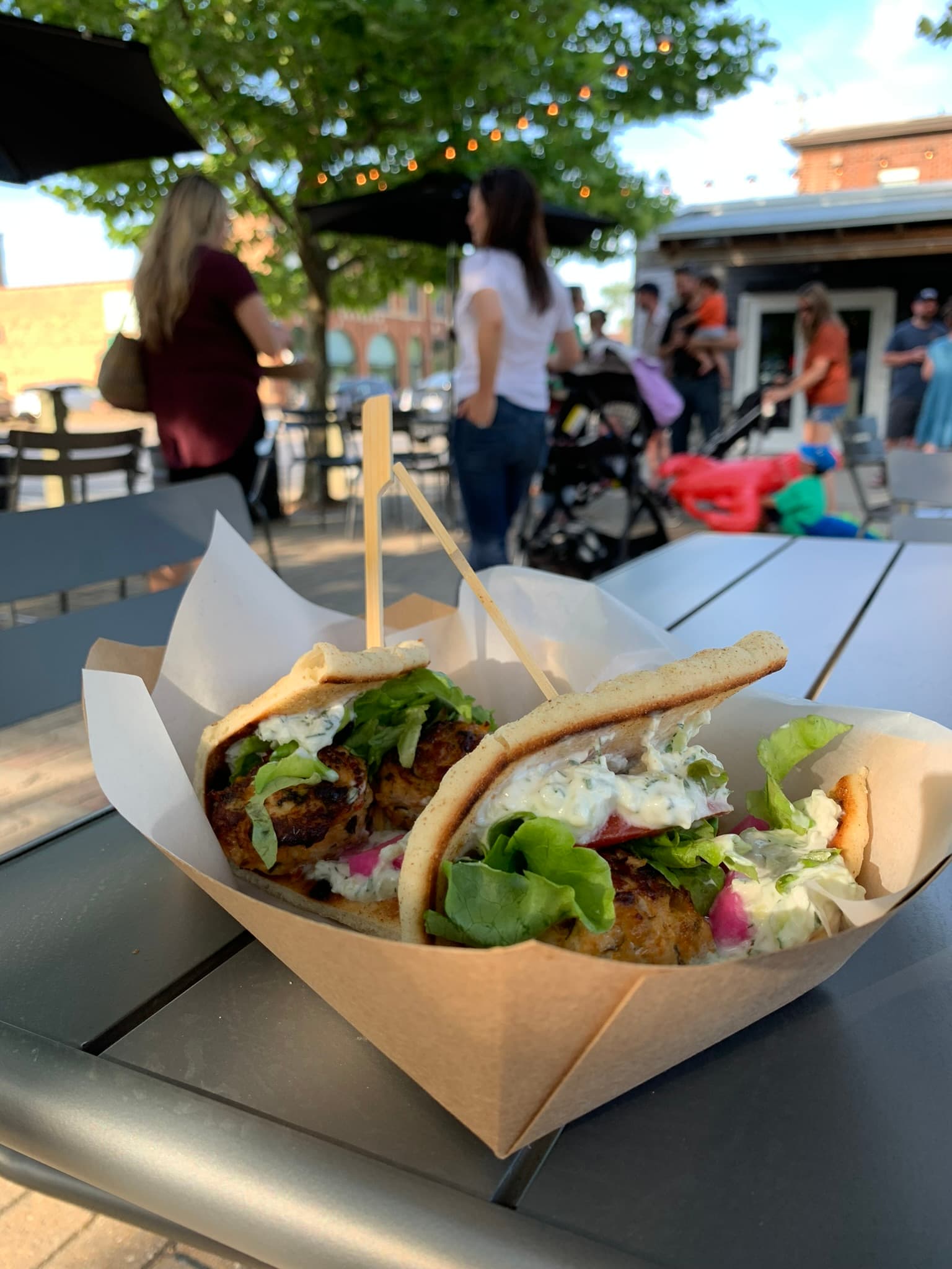 A close-up of two pita sandwiches filled with lettuce and sauces on a table, with people in the background.