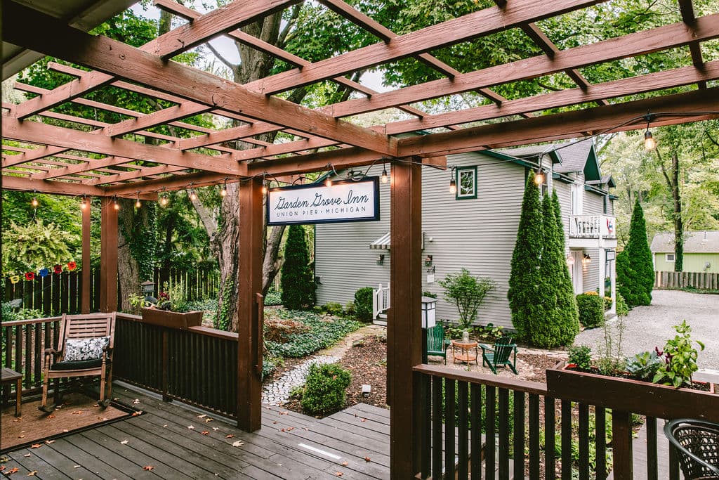 A cozy outdoor seating area with a wooden pergola and a sign for "Garden Grove Inn" surrounded by greenery.