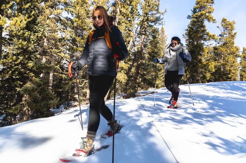 woman wearing snowshoes holding poles walking down a snow-covered hill woman wearing snowshoes holding poles walking down a snow-covered hill