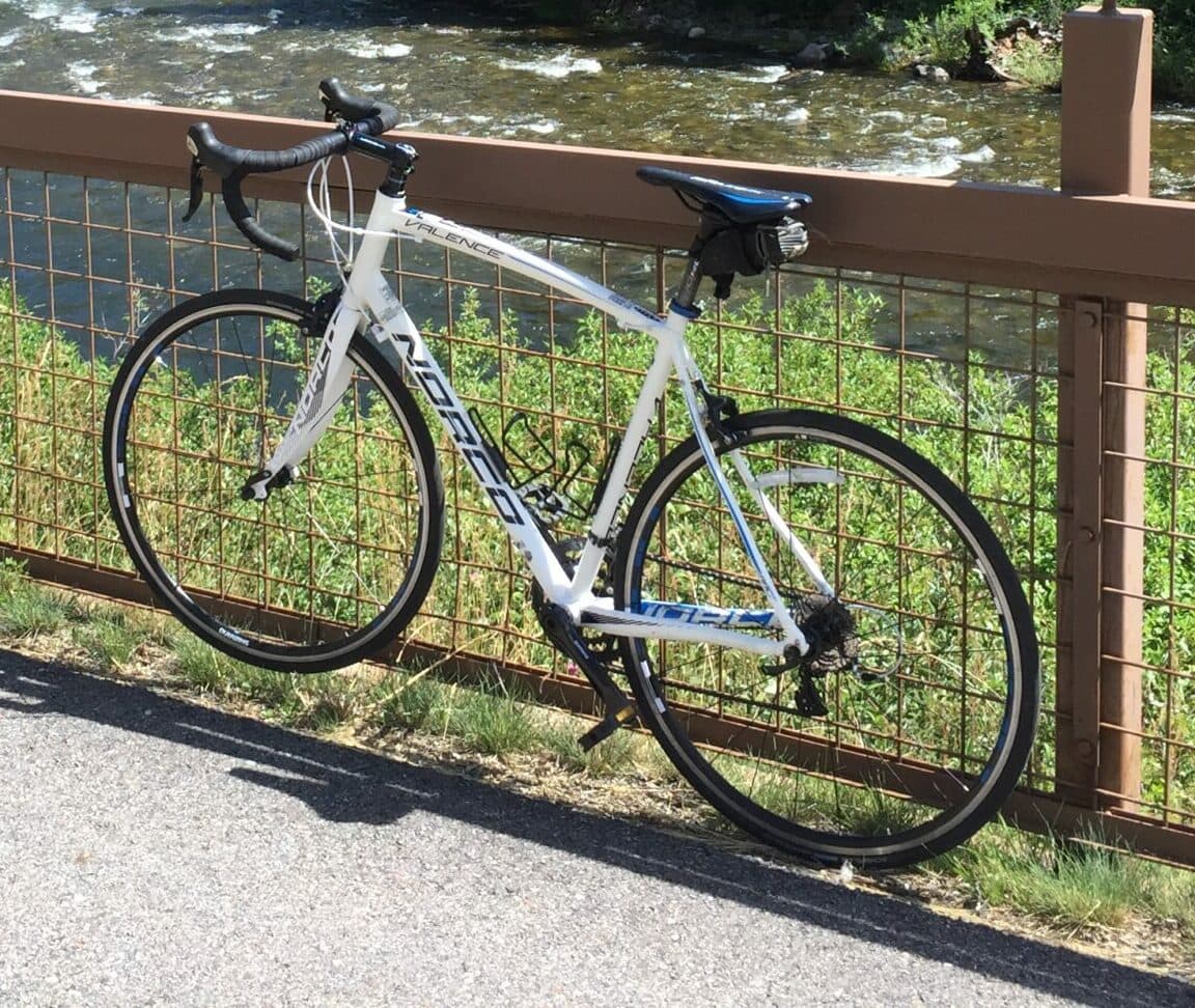 road bicycle secured to a metal fence next to a river